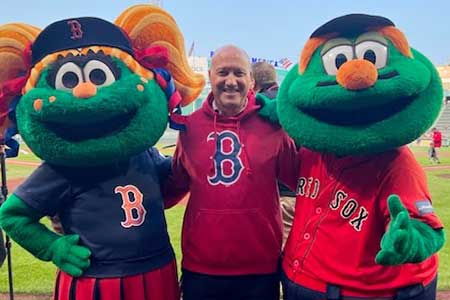 Principal Maguire stands between the two Red Sox mascots on the field at Fenway Park